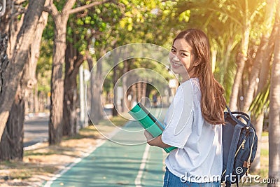 Cheerful attractive young woman with backpack and notebook and standing in the park Stock Photo