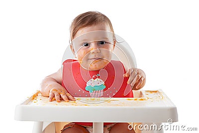 Cheerful baby child eats food itself with hands. Portrait of happy dirty kid boy in high chair and messy around Stock Photo