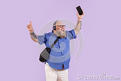 Plus size man with headphones enjoys music on mobile phone on purple background Stock Photo