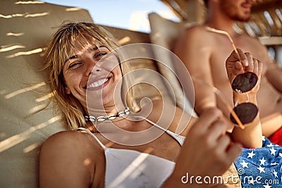 Cheerful beautiful woman lying on sunbed in shade on beach. Couple on summer holiday toghether. Love, togetherness, holiday, Stock Photo