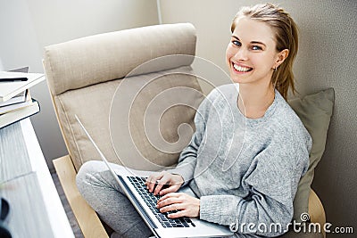 Cheerful blonde in gray home suit with laptop in her hands sitting in chair. Stock Photo