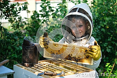 Cheerful boy beekeeper in protective suit near beehive. Honeycomb with honey. Organic food concept. The most useful Stock Photo