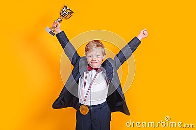 Cheerful boy holding a golden trophy and gold medal on yellow background Stock Photo