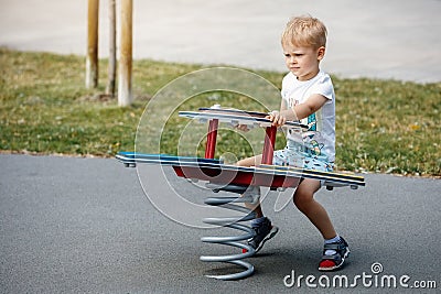 The cheerful boy springs up and balances on the swings of a modern outdoor playground Stock Photo