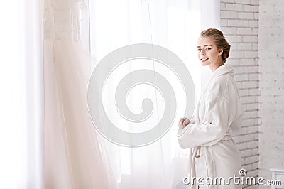 Cheerful bride standing near the window in the white room Stock Photo