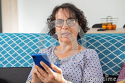 Cheerful brunette senior woman using smartphone while sitting on sofa Stock Photo