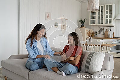Shy introverted teenage girl sits in closed position on couch with mother wanting to play together Stock Photo