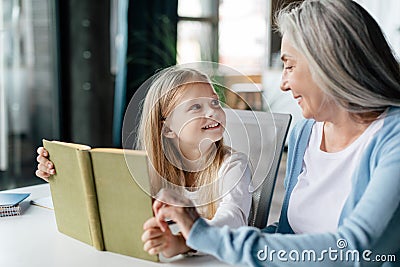 Cheerful caucasian little preschooler with aged grandma read book, enjoy study and free time in living room Stock Photo