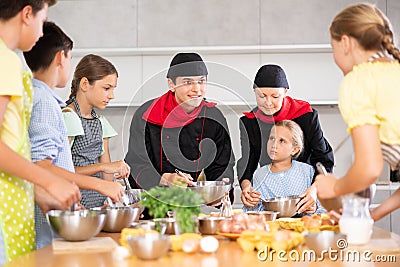 Cheerful chefs in black uniform conducting culinary masterclass for children Stock Photo