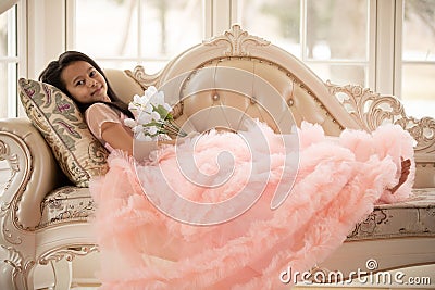Cheerful child wearing a colorful dress lying on an upholstered sofa in a relaxed, content posture Stock Photo