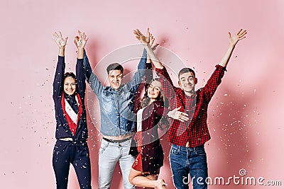 Cheerful company of two girls and two guys dressed in stylish clothes are standing and having fun with confetti on a Stock Photo