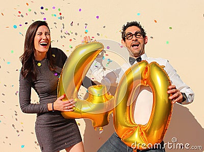 Cheerful couple celebrates a forty years birthday with big golden balloons and colorful little pieces of paper in the air Stock Photo