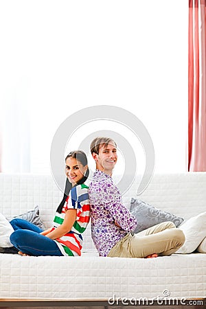 Cheerful couple sitting on sofa back to back Stock Photo