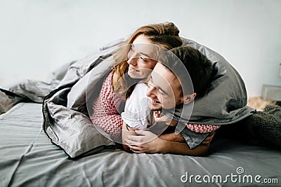 Cheerful couple under the coverlet in their bed. Artwork. Soft focus on the girl Stock Photo