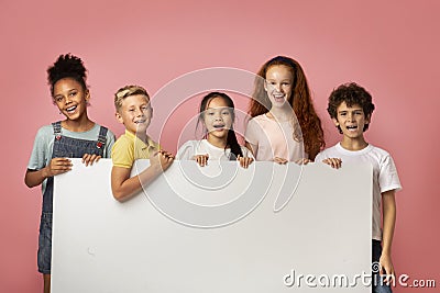 Cheerful diverse schoolkids holding blank banner with space for design over pink background Stock Photo