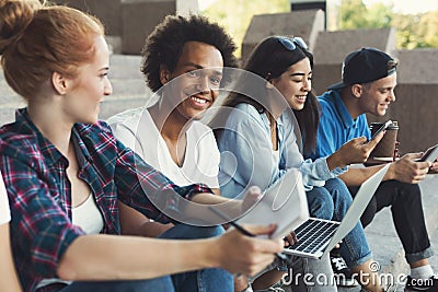 Cheerful diverse teens sitting outdoors and talking Stock Photo