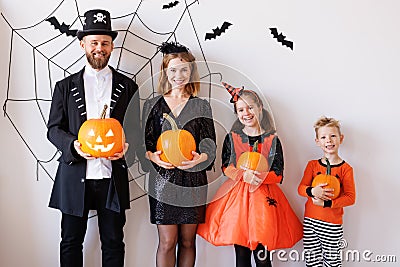 Cheerful family in carnival costumes celebrate Halloween near a gray wall with cobwebs and bats Stock Photo