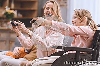 cheerful family with disabled child in wheelchair playing with joysticks together Stock Photo