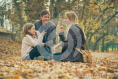 Cheerful family of three kneel on park ground covered with leaves Stock Photo