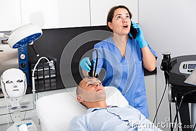 Female beautician talking on phone during facial treatment to client Stock Photo