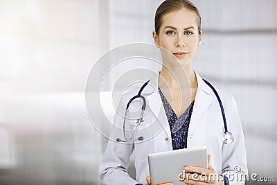 Cheerful female doctor standing in sunny clinic. Portrait of friendly smiling woman-physician. Medicine concept Stock Photo