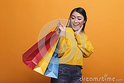 Cheerful friendly fashionable shopper smiling while carrying shopping bags and wearing yellow trendy sweater. Stock Photo