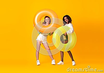 Cheerful friends woman dressed in summer clothes holding rubber ring over yellow background Stock Photo