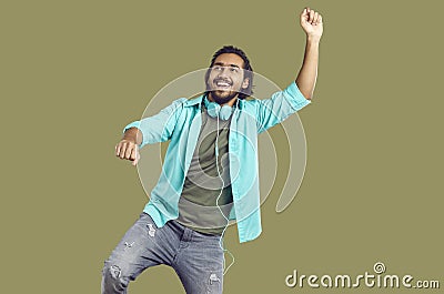 Cheerful funny indian man in headphones around his neck dancing and having fun on khaki background. Stock Photo