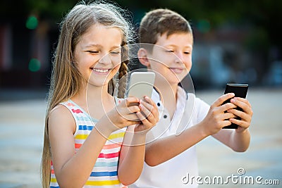 Cheerful girl and boy looking at mobile phones in park Stock Photo