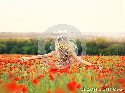 Cheerful girl with curly blond hair dances in a huge poppy field alone, her hair is flying because of the wind flow Stock Photo