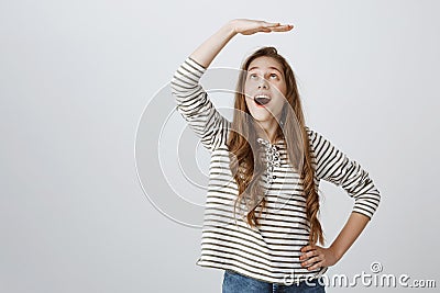 Cheerful girl dreams to become higher. Portrait of attractive playful woman raising palm above head as if measuring Stock Photo