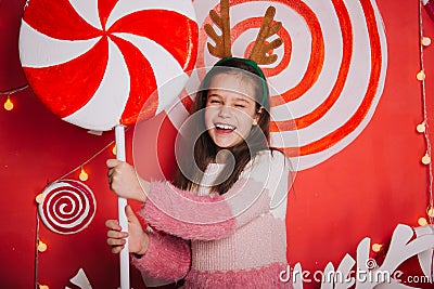 A cheerful girl with horns holds a candy in her hands. A wall of lollipops. Child stands against the background of New Year`s Stock Photo