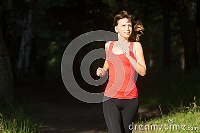 Cheerful girl jogging at morning in summer park. Smiling young caucasian woman dressed in sportwear run out from shadow of the for Stock Photo