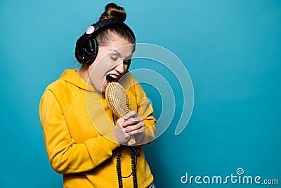A cheerful girl in large headphones expressively sings in a hairbrush, fools around Stock Photo