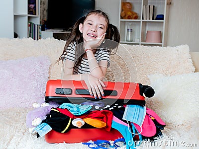 A cheerful girl leaned on a red suitcase that does not close because of a large number of things. Opening of borders. A Stock Photo