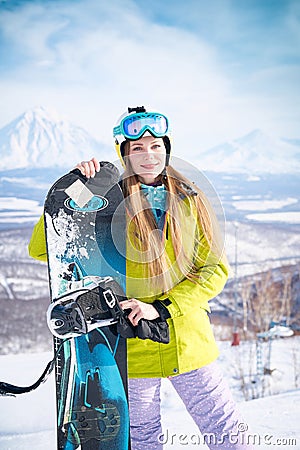 Cheerful girl snowboarder in green jacket in front of peaks snowy volcanos Stock Photo