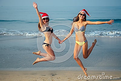 Cheerful girlfriends in a santa hat and bikini jumping on the beach Stock Photo