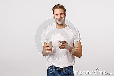 Cheerful good-looking modern blond man with bristle, holding paper cup of coffee, drinking tea and holding smartphone Stock Photo