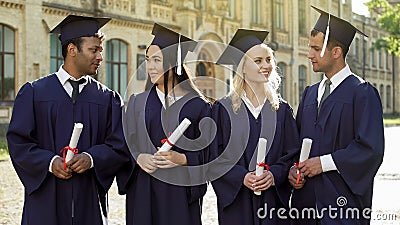 Cheerful graduate students in academic regalia talking to each other, success Stock Photo