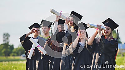 Cheerful graduates on a sunny day look through diplomas like a telescope. Stock Photo