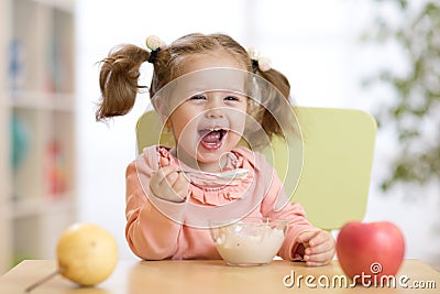 Cheerful baby child eating food itself with a spoon Stock Photo