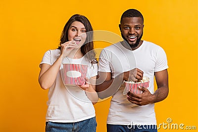 Cheerful interracial couple eating popcorn, enjoying cinema snack over yellow background Stock Photo
