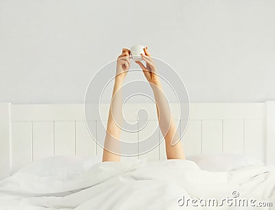 Cheerful lazy woman waking up after sleeping lying in soft comfortable bed showing empty cup coffee stretching her hands up from Stock Photo