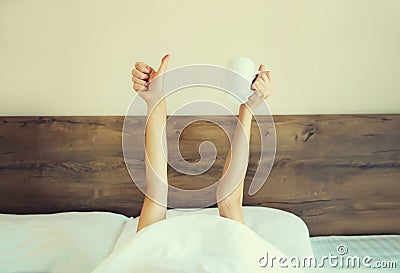 Cheerful lazy woman waking up after sleeping lying in soft comfortable bed showing empty cup coffee stretching her hands up from Stock Photo