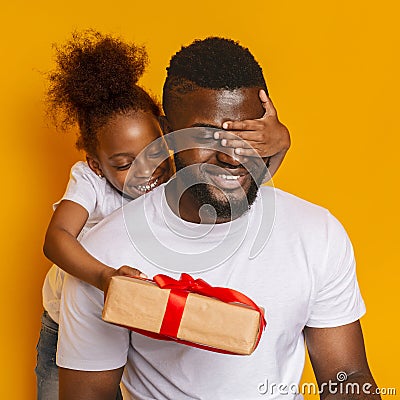 Cheerful little afro daughter closing dad eyes and giving gift box Stock Photo