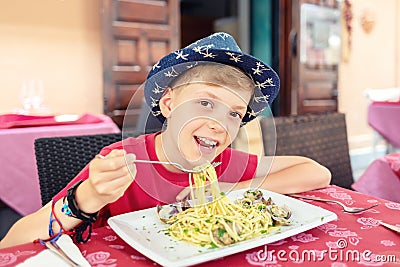 Cheerful little boy enjoying eating italian food - Portrait of happy smiling kid eating seafood pasta for lunch Stock Photo