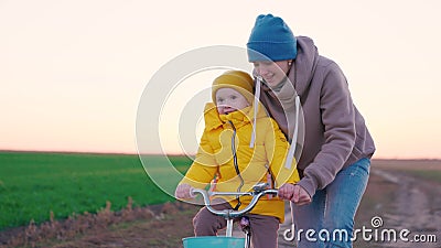 cheerful little child with her mother learns ride two-wheeled bike sunset, happy family, pedal and wheel, mom help kid Stock Photo