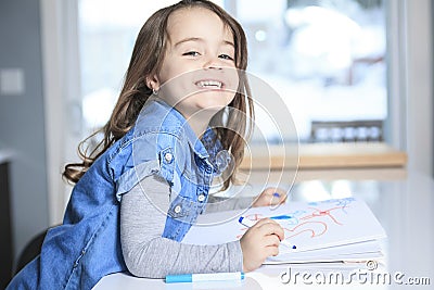 Cheerful little girl colouring at the table at Stock Photo