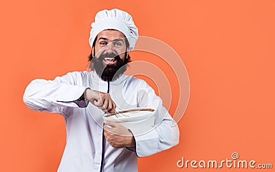 Cheerful male chef in hat with beard and moustache on orange background beating meal with beater, cuisine, copy space Stock Photo