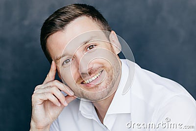 Cheerful male employee has joyful expression, keeps finger on temple, rejoices starting vacation, dressed in formal white shirt, p Stock Photo